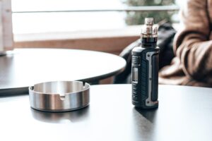 Modern vape mod device on café table next to metal ashtray
